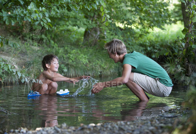Friends playing with boat in stream, smiling — Stock Photo