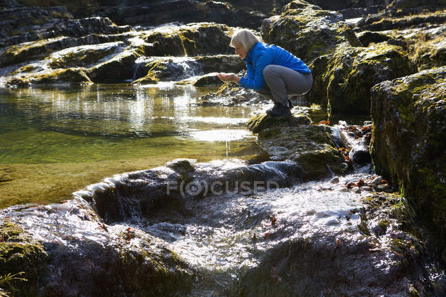 Austria, Land Salzburgo, Faistenau, Mujer madura bebiendo agua del río - foto de stock