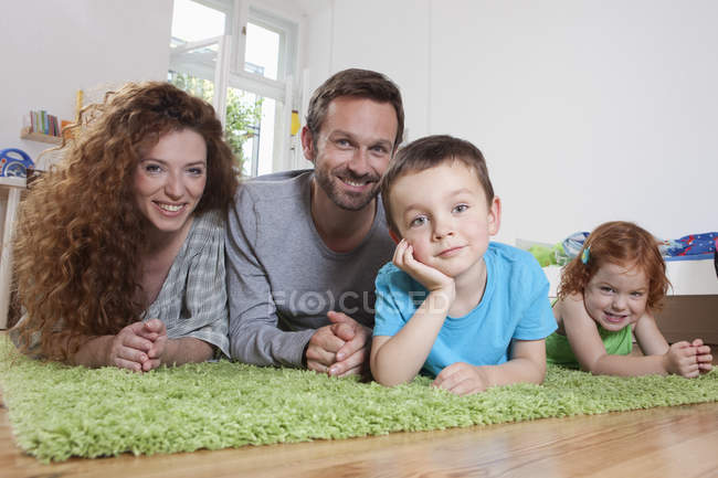 Усміхаючись сім'ї, відпочиваючи на підлозі і, дивлячись на камеру — стокове фото
