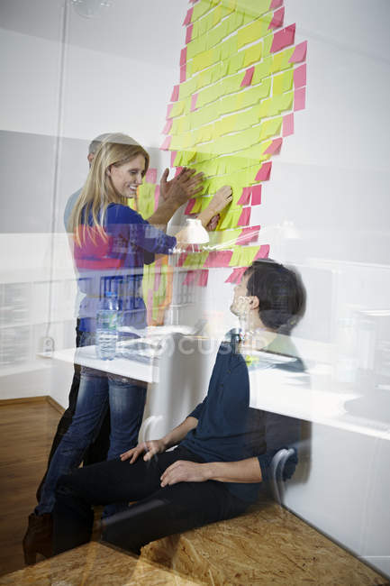 Hommes et femmes collant note de papier sur le mur dans le bureau moderne — Photo de stock