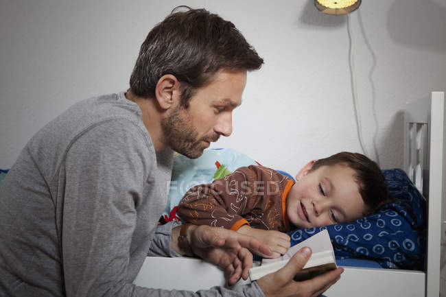 Padre leyendo libro mientras hijo durmiendo - foto de stock