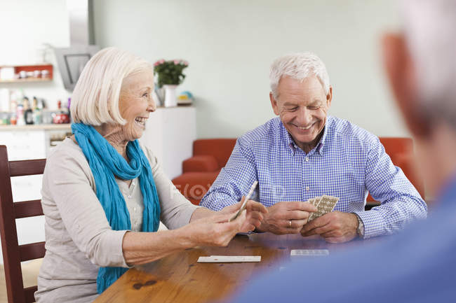 Uomini e donne anziani che giocano a carte, sorridendo — Foto stock
