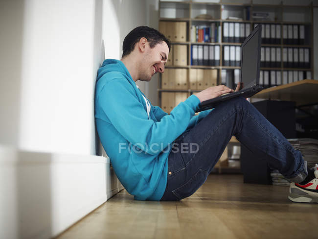 Jeune homme utilisant un ordinateur portable assis sur le sol — Photo de stock