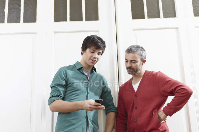 Uomo che utilizza il telefono cellulare vicino alla porta di casa — Foto stock