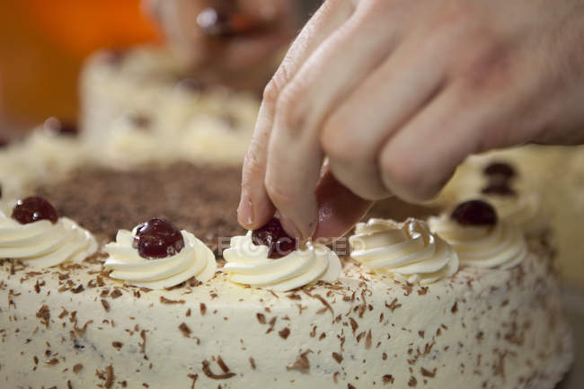 Baker decorating cake with cherry, close up — Stock Photo