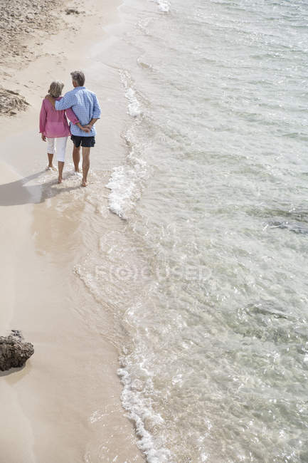 Старшая пара, идущая вдоль пляжа держась за руки — стоковое фото