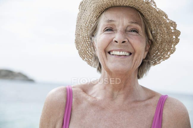 Femme âgée avec chapeau de paille sur la plage — Photo de stock