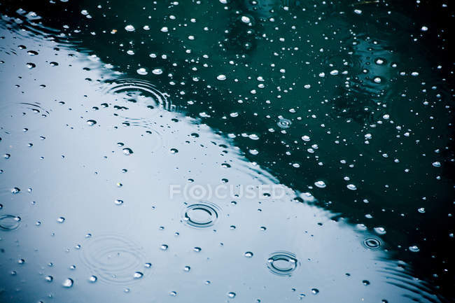 Raindrops falling on puddle, partial view — Stock Photo
