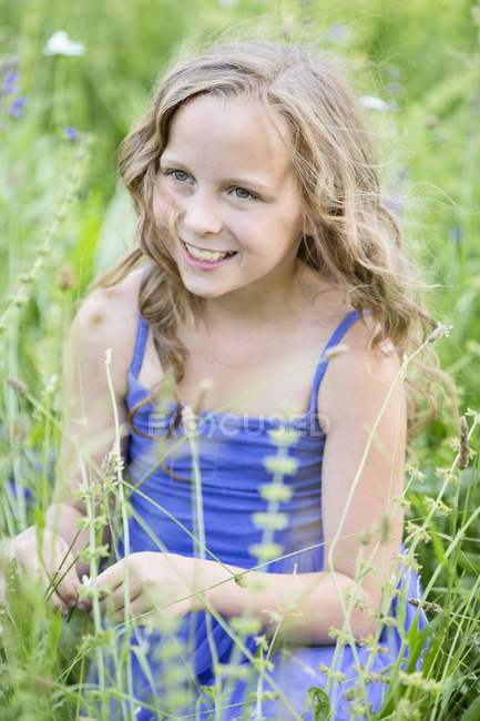 Портрет улыбающейся девушки, сидящей на цветочном лугу — стоковое фото