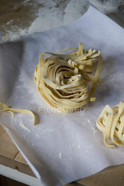 Fresh unwrought tagliatelle and flouron baking paper — Stock Photo