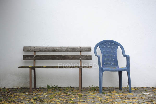 Banco de madera y una silla de jardín de plástico azul en frente de la pared blanca - foto de stock