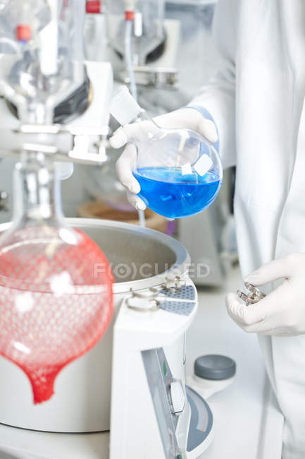 Giovane scienziato maschio che esamina il liquido blu sull'evaporatore rotante in laboratorio — Foto stock
