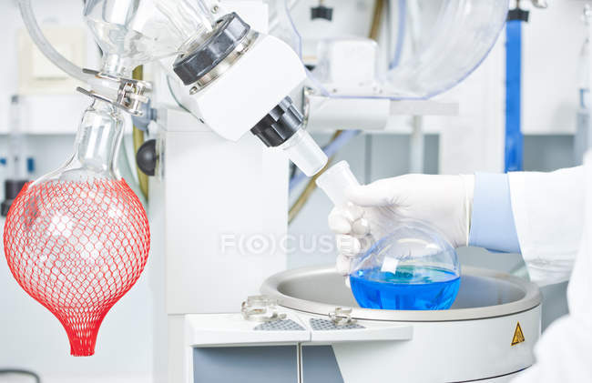 Jovem cientista examinando líquido azul em evaporador rotativo em laboratório — Fotografia de Stock