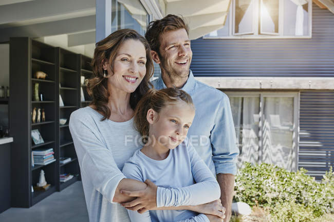 Familia feliz de pie en la terraza, abrazando a la hija - foto de stock