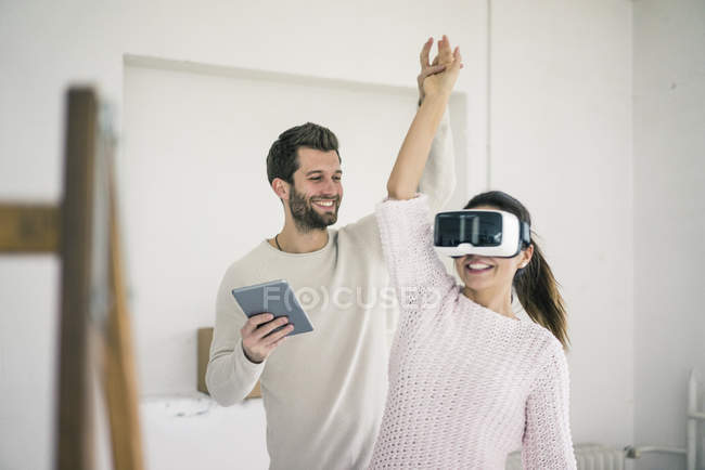 Homem levantando braço mulher enquanto ela vestindo óculos VR em nova casa — Fotografia de Stock