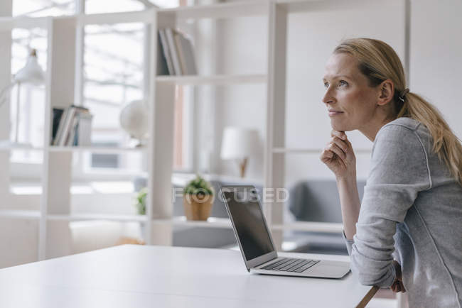 Femme avec ordinateur portable assis au bureau et pensant — Photo de stock
