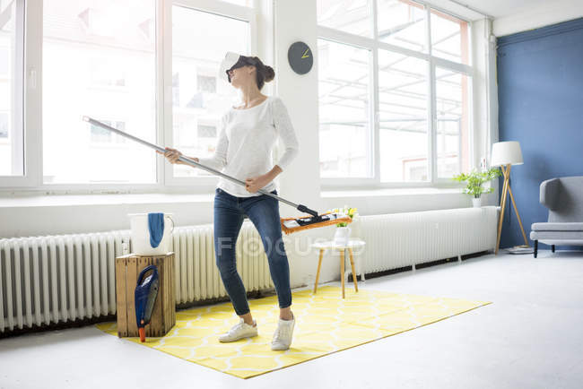 Жизненно важная женщина дома в VR очках и вытирает пол — стоковое фото