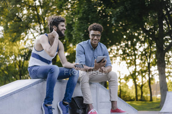 Due amici multiculturali felici seduti nello skatepark con dispositivi mobili — Foto stock