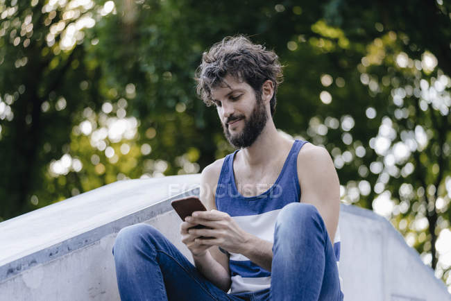 Людина з мобільного телефону сидять в скейтпарк — стокове фото