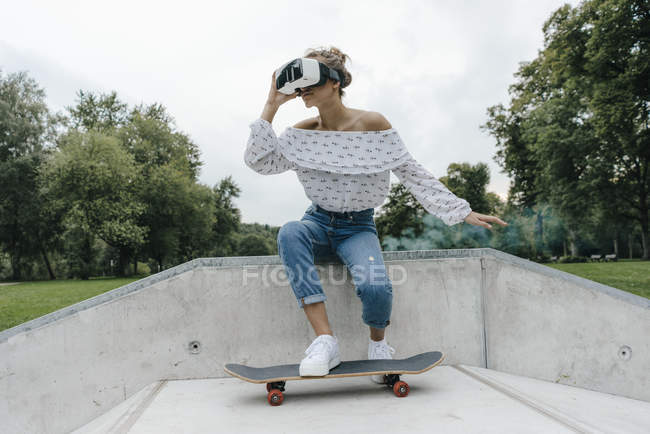 Young woman with skateboard wearing VR glasses in a skatepark — Stock Photo