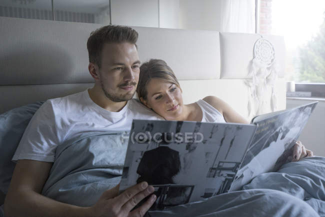 Пара в ліжку в будинку, дивлячись на весілля каталог — стокове фото