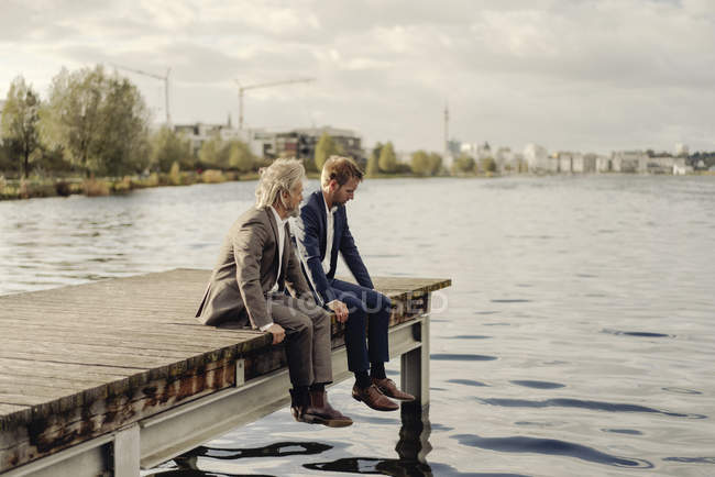 Dois homens de negócios sentados no cais no lago — Fotografia de Stock