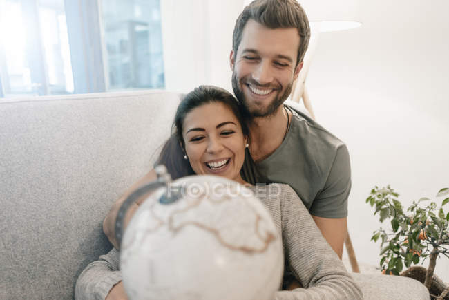 Feliz pareja en sofá en casa mirando globo - foto de stock