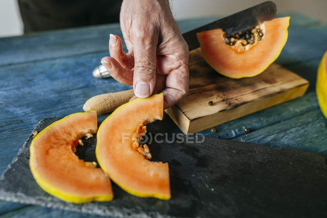 Primer plano de las manos del hombre la colocación de piezas de papaya en la placa de pizarra - foto de stock