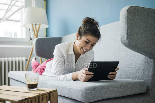 Retrato de la mujer riendo relajándose en el sofá con la tableta - foto de stock