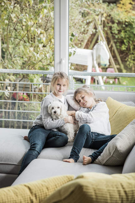 Portrait de deux filles avec chien sur canapé dans le salon — Photo de stock