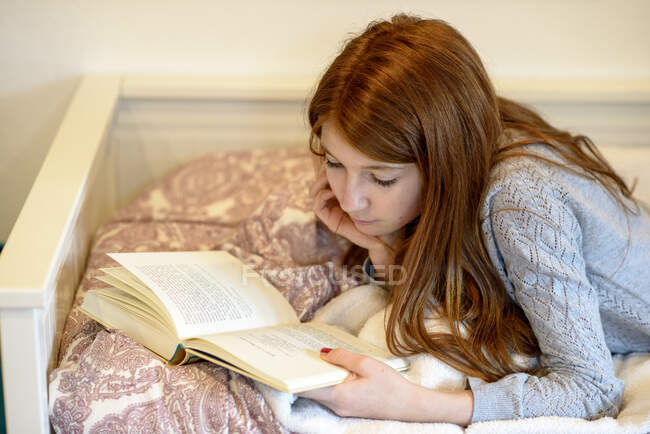 Ruiva adolescente deitada na cama lendo um livro — Fotografia de Stock