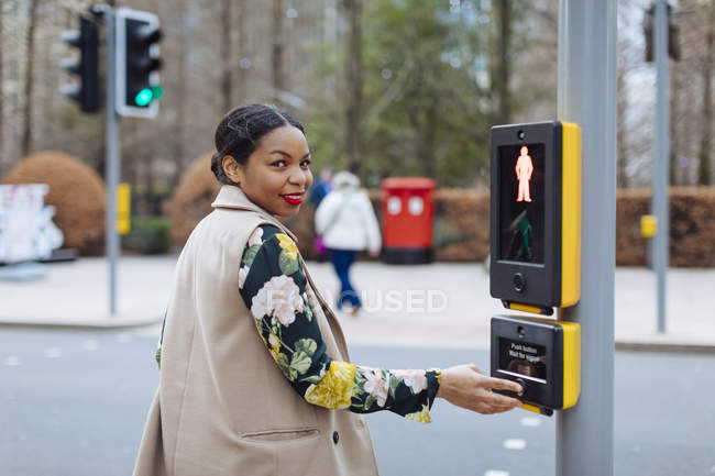 Reino Unido, Londres, retrato de la mujer sonriente pulsando el botón de la luz peatonal - foto de stock