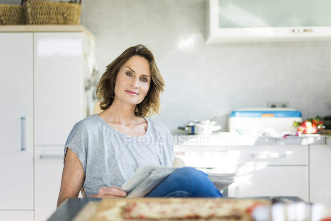 Portrait of woman with newspaper in kitchen at home — Stock Photo