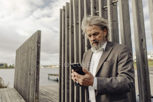 Uomo anziano che usa il cellulare sul lungolago — Foto stock