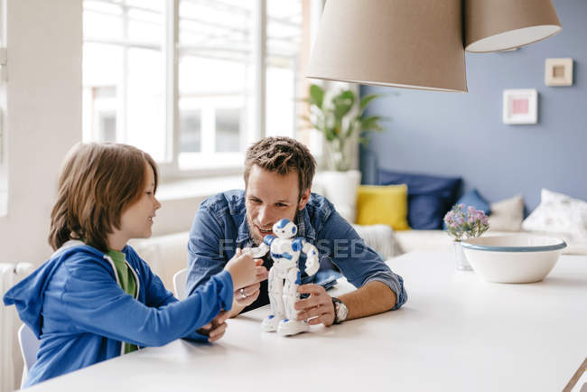 Счастливые отец и сын играют с роботом на столе дома — стоковое фото
