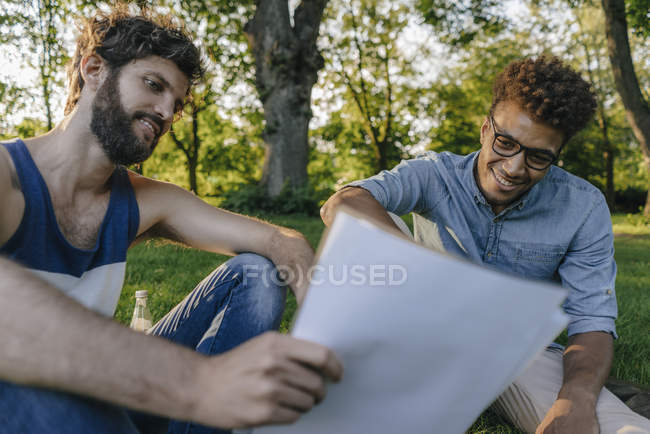 Два мультикультурных друга сидят в парке и обсуждают документы — стоковое фото