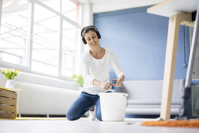 Mulher sorridente em casa usando fones de ouvido e limpando o chão — Fotografia de Stock