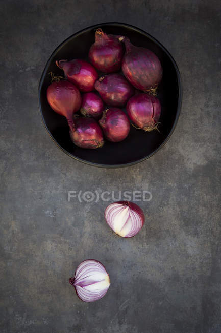 Fresh pink onions in bowl on grey surface with halves — Stock Photo
