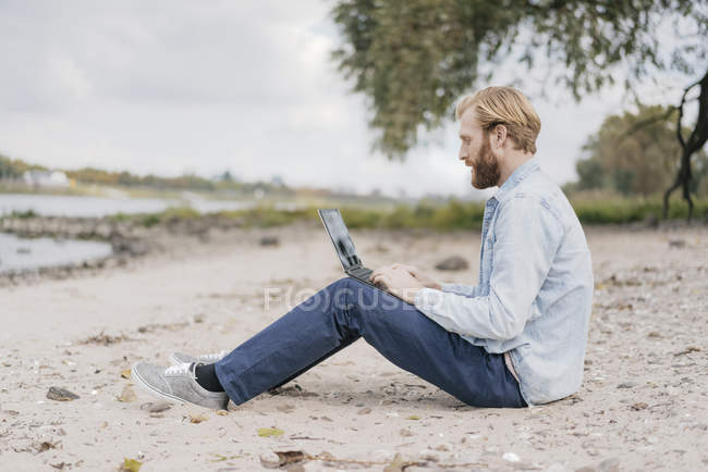 Homme assis sur la plage et utilisant un ordinateur portable — Photo de stock