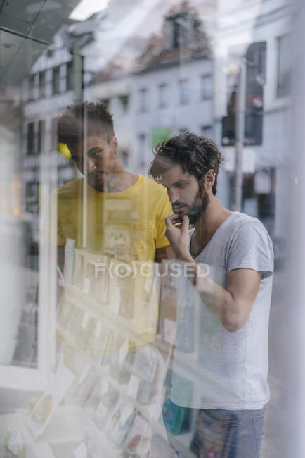 Dos amigos multiculturales mirando en la ventana de la librería en la ciudad - foto de stock