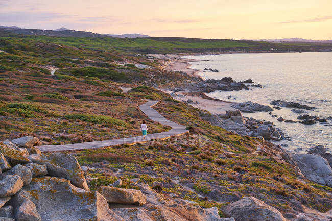 Italia, Sardegna, Lu Litarroni, donna anziana che cammina sul lungomare di legno al tramonto — Foto stock