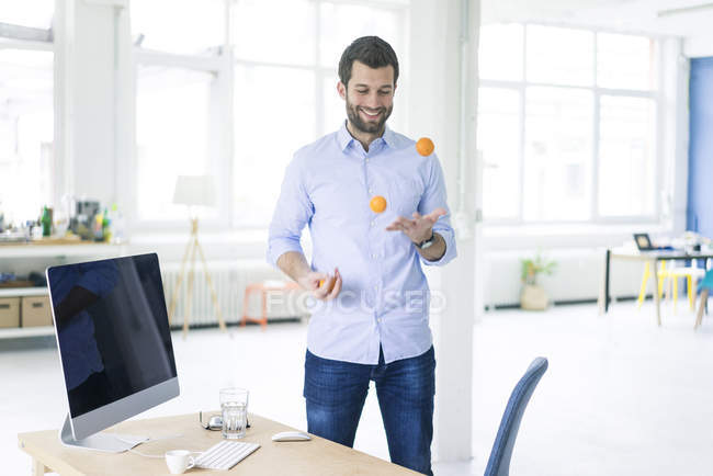 Smiling businessman juggling with tangerines in office — Stock Photo