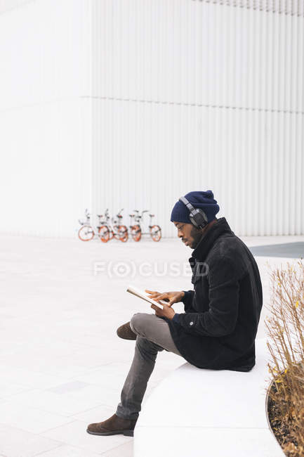 Италия, Милан, африканский мужчина с книгой для чтения в наушниках — стоковое фото