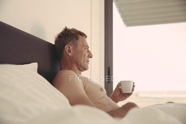 Uomo rilassato a letto in possesso di una tazza di caffè — Foto stock