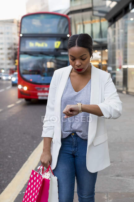 UK, London, woman with shopping bags in the city checking the time — Stock Photo