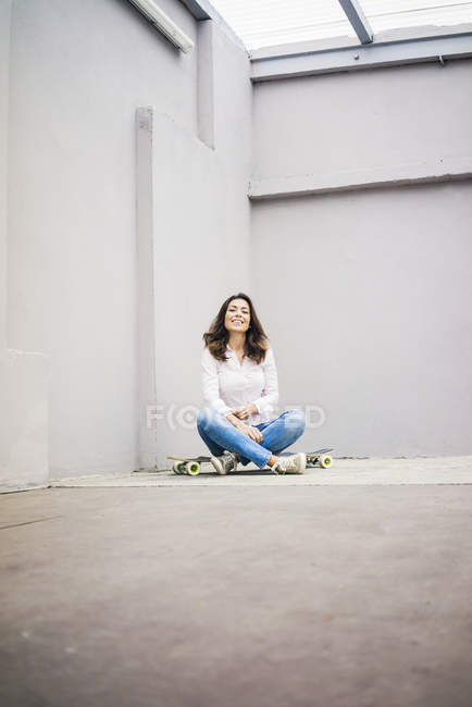 Улыбающаяся молодая женщина сидит на скейтборде на террасе — стоковое фото