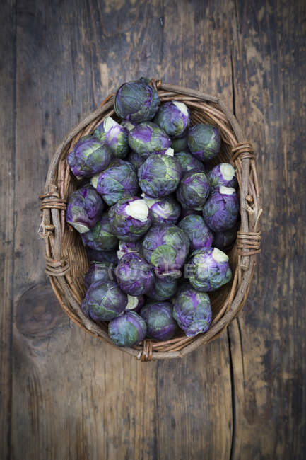 Purple brussels sprouts in basket on rustic wooden table — Stock Photo