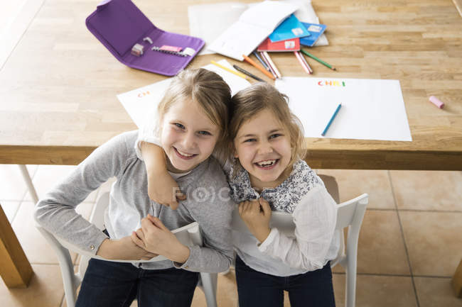 Retrato de dos chicas felices abrazándose juntas en la mesa - foto de stock