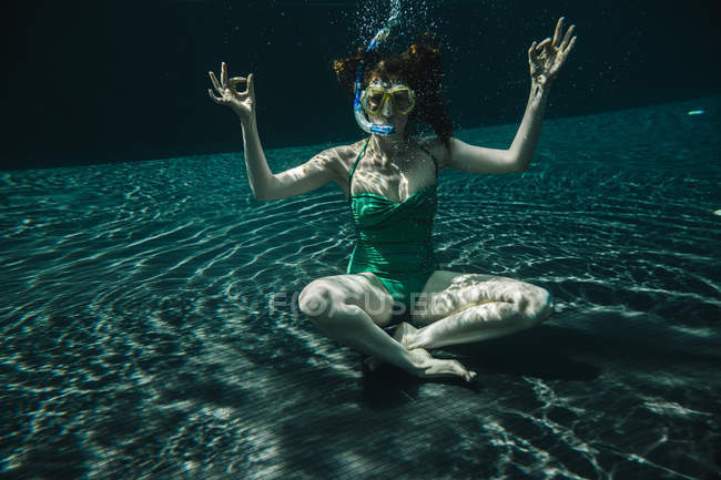 Donna con occhiali subacquei e snorkeling seduta in posa yoga sott'acqua in piscina — Foto stock