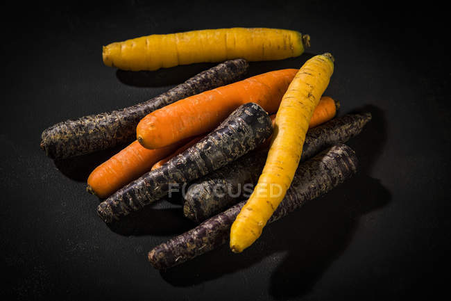 Свежая оранжевая и фиолетовая морковь на черном фоне — стоковое фото